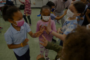 Students wear masks while clapping hands in school.