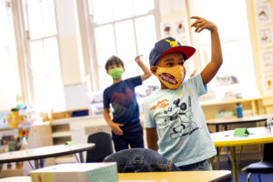 Students raise their hands and enjoy music class while wearing protective masks.