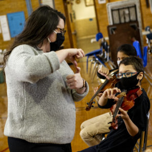 A music teacher instructs a student on how to pluck violin strings.