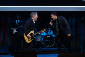 Andy hilfiger plays guitar on stage with high school student singer